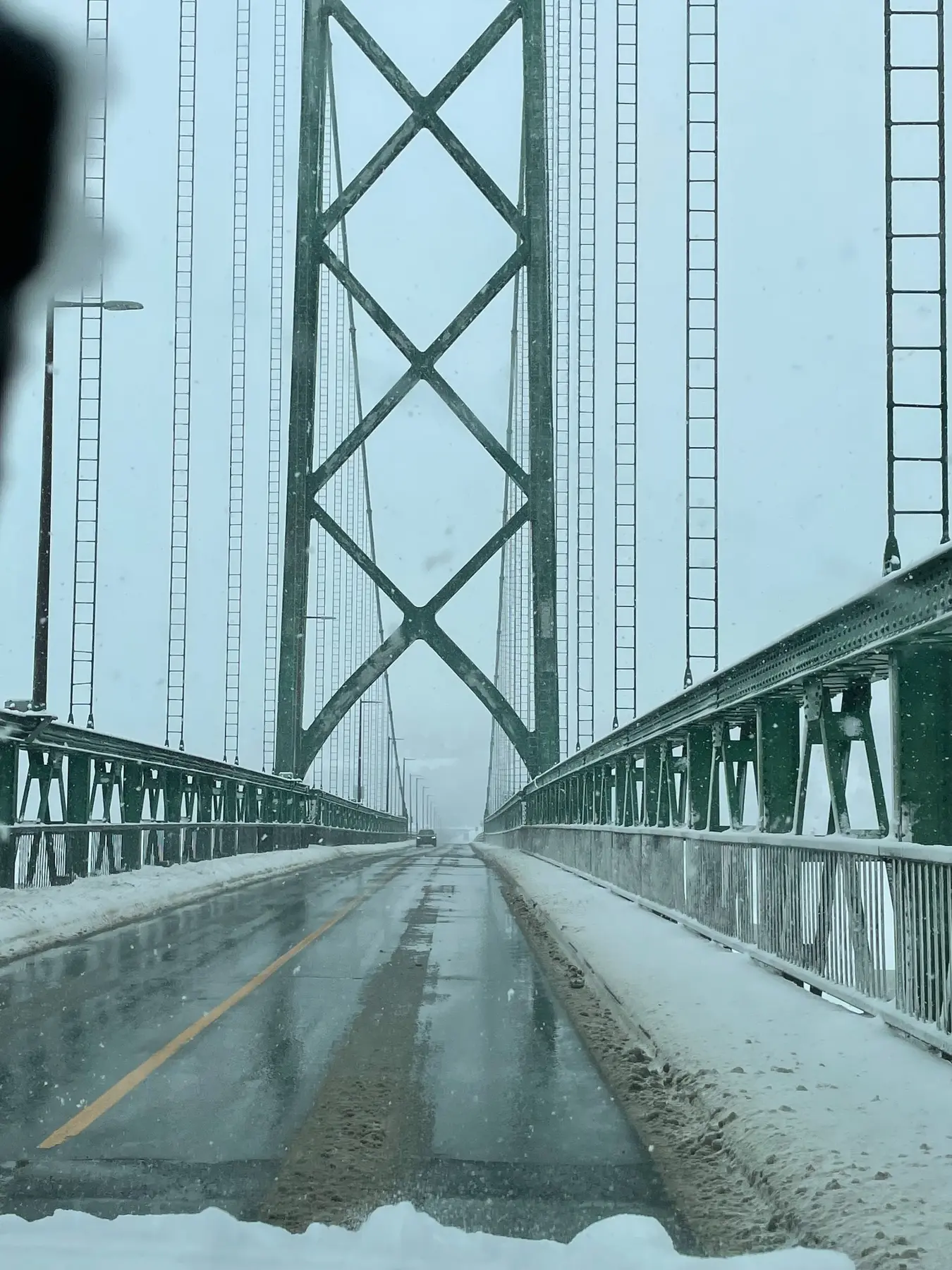 Green suspension bridge viewed from a snow-covered road